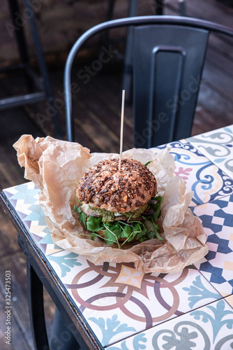 Świeżo grillowany burger leży na stoliku azelejos. Kanapka w amerykańskim stylu zawinięta w papier ekologiczn, street food. Restauracja w industrialnym stylu. 
