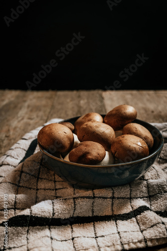 Stock photo of group of Shiitake mushrooms inside blue bowl on tablecloth and natural wooden table with black background.