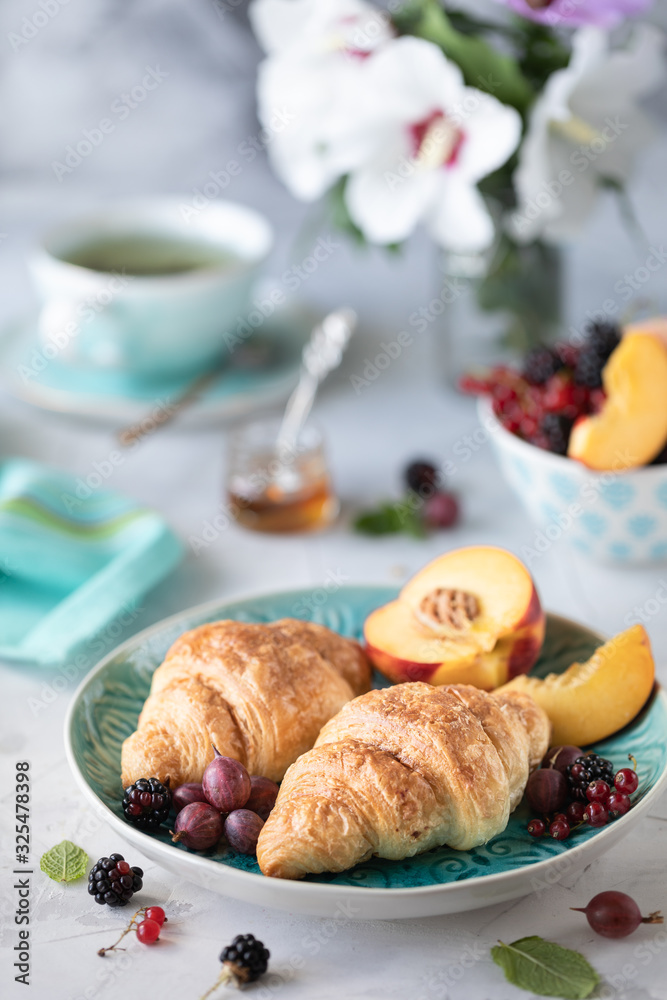 Breakfast of fresh berries and fruits with croissants, teas a bouquet of summer flowers. Vertical