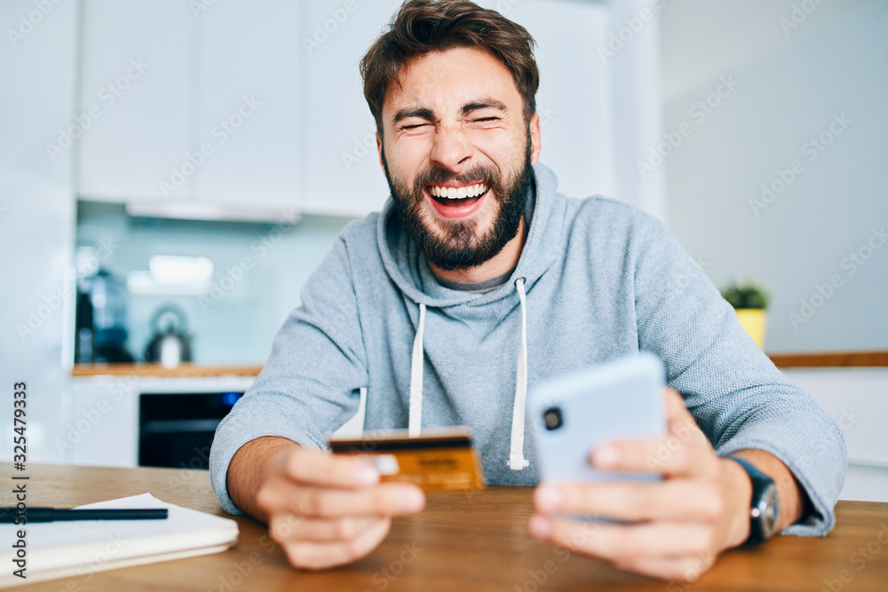 Young man screaming in joy while shopping online with smartphone and credit card Young man screaming in joy while shopping online with smartphone and credit card