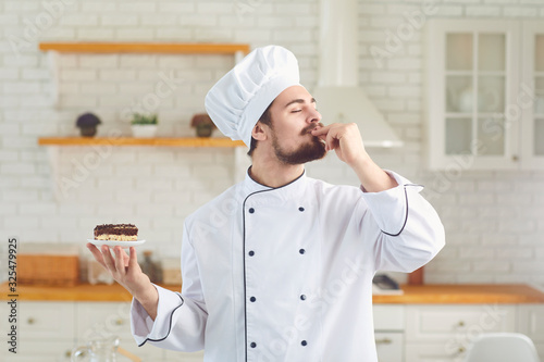 Confectioner man smiles while standing with cake in his hands at the kitchen bakery photo