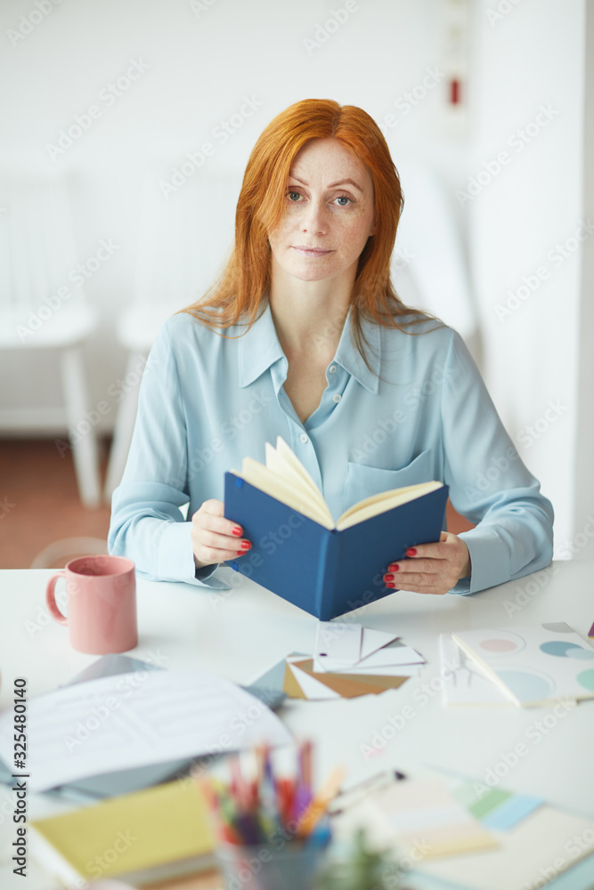 Portrait of freckled young woman looking at camera while holding planner at designers workplace Portrait of freckled young woman looking at camera while holding planner at designers workplace
