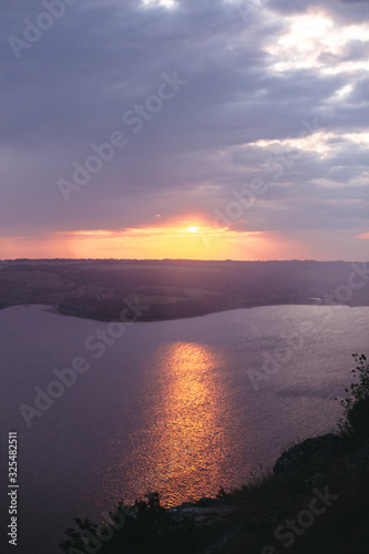 Beautiful view of sunset warm light from dark clouds above lake. Sunny rays over hill and river landscape. Dramatic moody scenery. Bakota lake and Dniester river in Ukraine