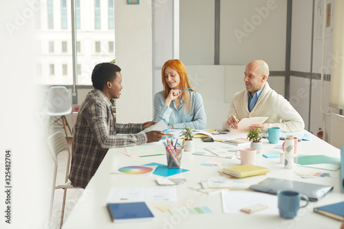 Portrait of mature business people smiling cheerfully while talking to African-American intern during interview meeting in modern white office, copy space