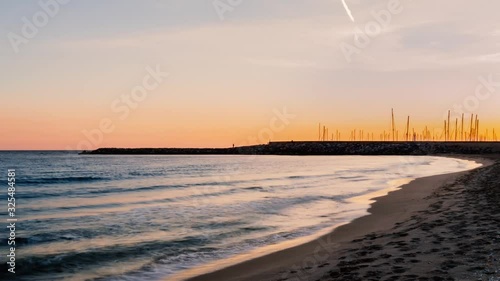Beautiful timelapse of the coastal sunset with yellow and orange colors in the sky with a port in the background.