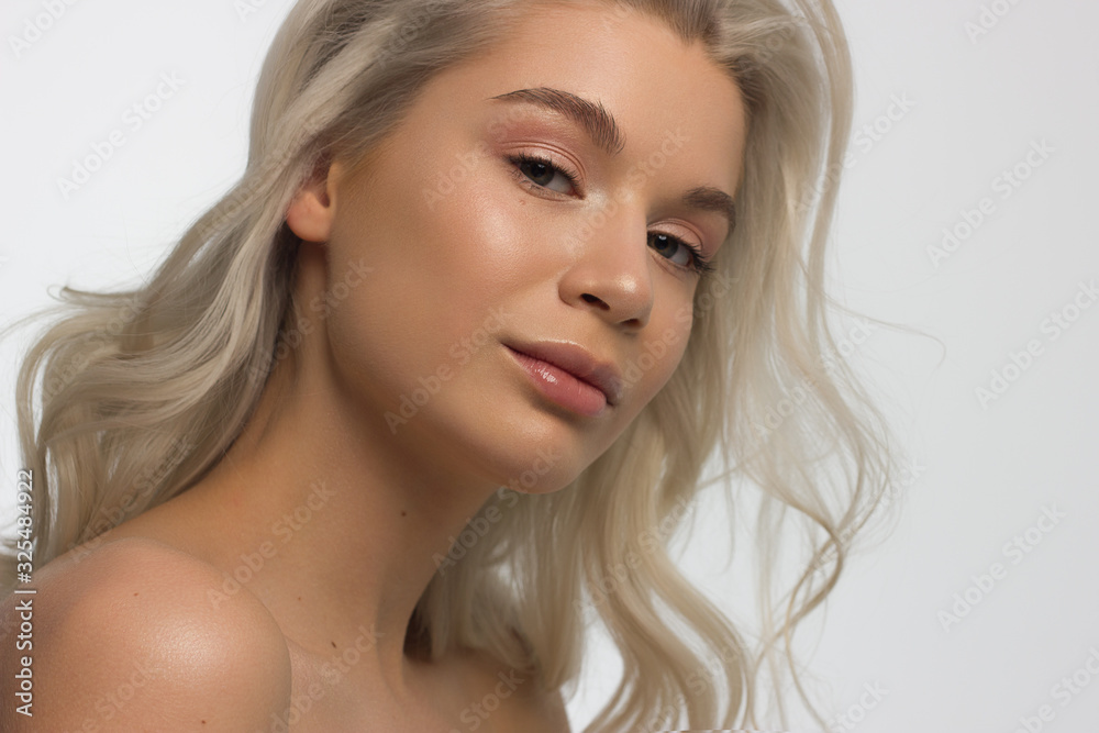 Fototapeta premium Closeup portrait of a woman with developing straight hair. Sweet tender young girl blonde. Natural lipstick, transparent clean skin. Skin care natural cosmetics in the spa salon or cosmetology.