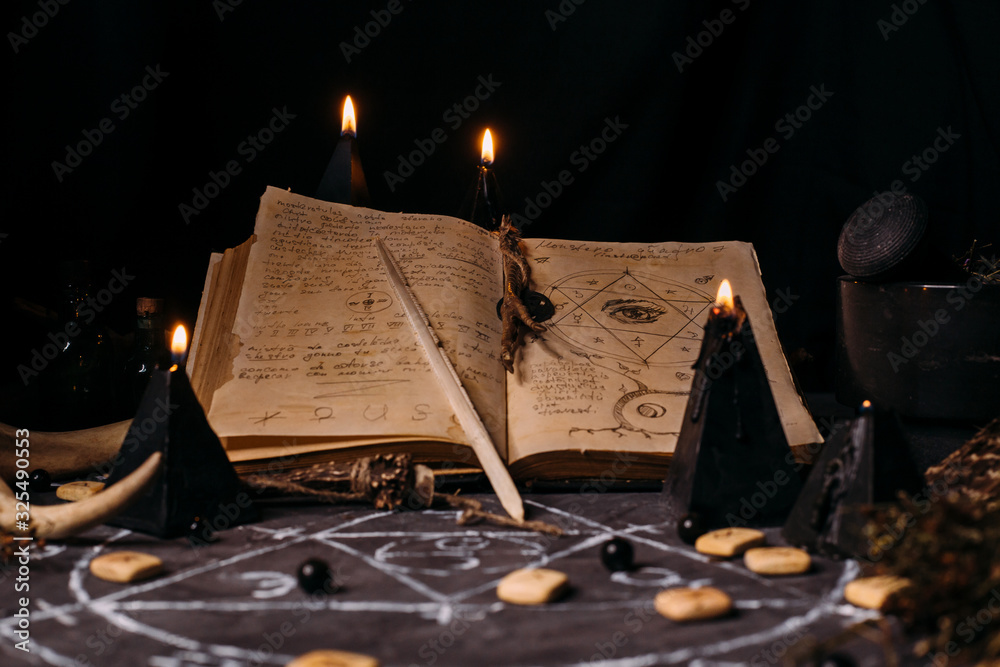 Open old book with magic spells, runes, black candles on witch table. Occult, esoteric, divination and wicca concept. - obrazy, fototapety, plakaty 