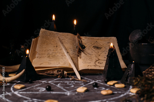 Obraz na płótnie Open old book with magic spells, runes, black candles on witch table