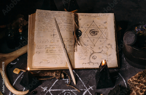 Photo Open old book with magic spells, runes, black candles on witch table