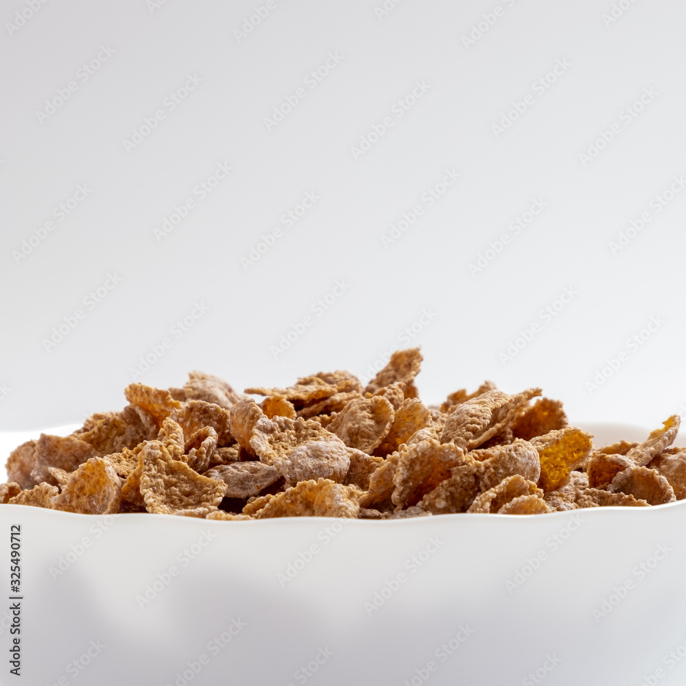 Natural whole grain wheat flakes in white bowl. Healthy breakfast concept. Plate with multigrain flakes on white background Natural whole grain wheat flakes in white bowl. Healthy breakfast concept. Plate with multigrain flakes on white background