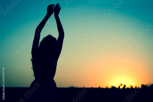  Silhouette of a woman hands up against a blue sky. Sunset or dawn. The concept of harmony and health woman