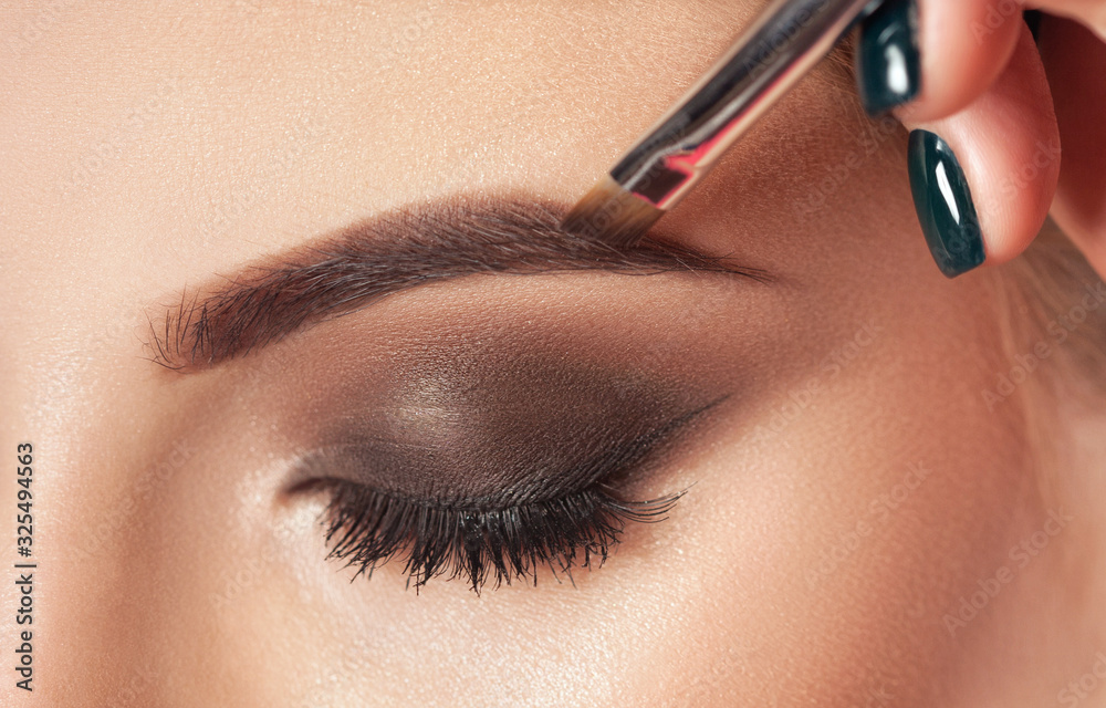 Make-up artist does eyebrow make-up to a woman with smoky eyes makeup. Beautiful thick eyebrows close up. Professional makeup and cosmetology skin care. - obrazy, fototapety, plakaty 