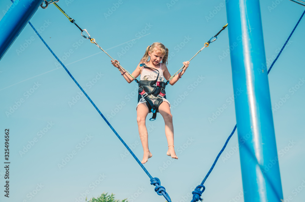 lovely blond caucasian girl jumping in the jump attraction in the playground