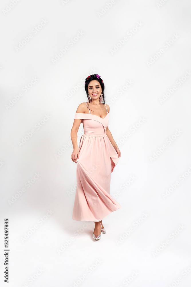 Full length portrait of cute young brunette woman wearing trendy pink dress with a spring hoop with flowers on her head. Studio shot on white background. Full length portrait of cute young brunette woman wearing trendy pink dress with a spring hoop with flowers on her head. Studio shot on white background.