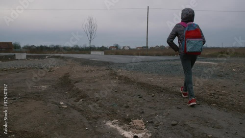 Anonymous young poor girl going to school in a village. photo