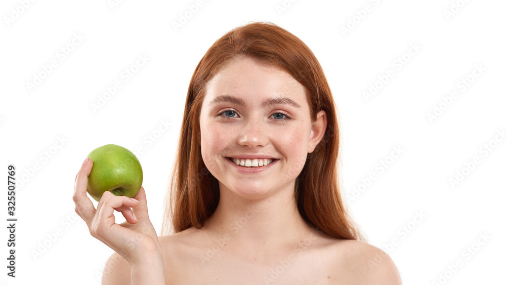 Only healthy food. Portrait of young and happy red-haired girl holding a fresh green apple and smiling while standing against white background Only healthy food. Portrait of young and happy red-haired girl holding a fresh green apple and smiling while standing against white background