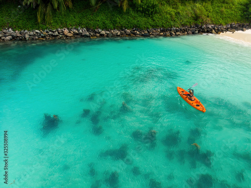 Aerial view of woman kayaking in a lagoon in Mahe, Seychelles. Top view of woman floating on orange kayak near a tropical beach