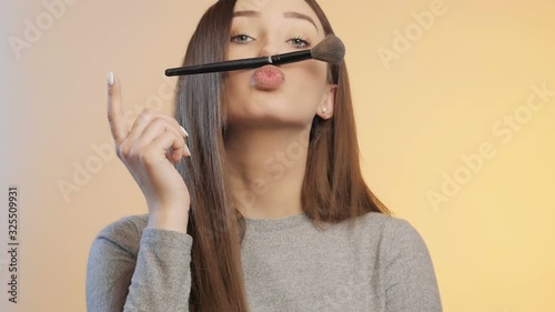 funny girl grimaces and fooling around with a makeup brush on a colored studio background, young woman in a positive mood, female beauty concept