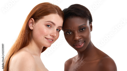 Milk and chocolate. Two multicultural young women with soft glowing skin looking at camera and smiling while posing in studio over white background. African and caucasian women standing together