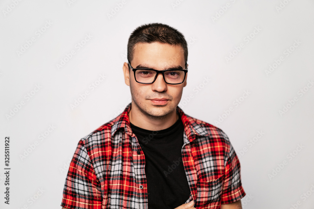 Close-up of young trendy guy with glasses smiling, white studio shot. A portrait of clever man in t-shirt looking at camera through new eyeglasses and testing them. Close-up of young trendy guy with glasses smiling, white studio shot. A portrait of clever man in t-shirt looking at camera through new eyeglasses and testing them.