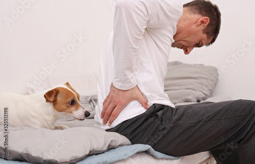 Man with back pain sitting on bed at home. Pain relief concept.