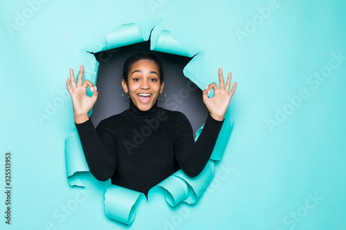 Young smile latin woman with okay gesture posing from green paper hole