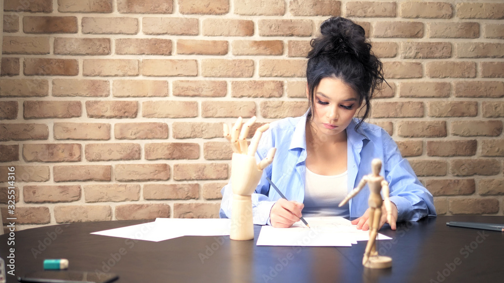 beautiful brunette girl draws a sketch with a wooden mannequin