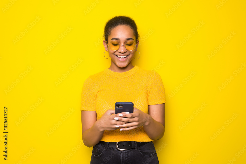 Photo of latin young woman chatting by mobile phone isolated over yellow background. Photo of latin young woman chatting by mobile phone isolated over yellow background.