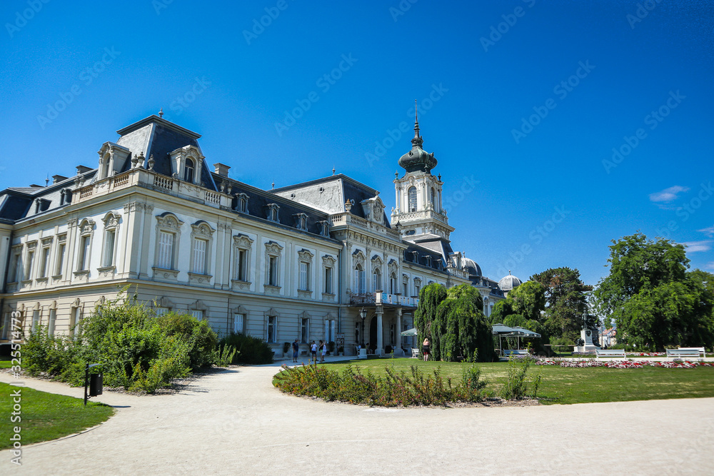Festetics Palace behind beautiful gardens in Keszthely, Hungary on a clear sunny day. view of the palace and gardens, and some tourists people.