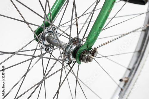 An old retro looking green vintage city bicycle for women, isolated o white background. Detail of front wheel hub with some rust, and nut on an axle.
