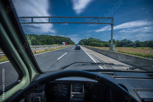 View from behind the steering wheel of an old van or lorry on a motorway or highway with low traffic on a sunny day and blue sky.