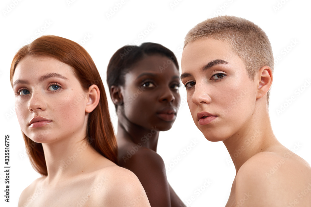 Portrait of three beautiful multicultural young women with naked shoulders posing in studio over white background. Beautiful models with black, red and blonde hair standing together Portrait of three beautiful multicultural young women with naked shoulders posing in studio over white background. Beautiful models with black, red and blonde hair standing together