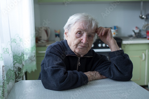Portrait of an elderly old woman sitting at the table in kitchen.