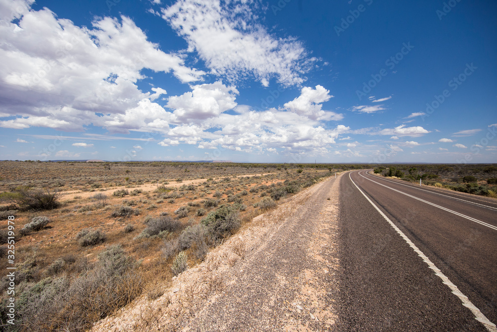 The road to nowhere at the Australian Outback. The stuart highway on the way to the Uluru or Ayers Rock. Empty street through the wide open flat australian outback. Wide angle shot over the  landscape