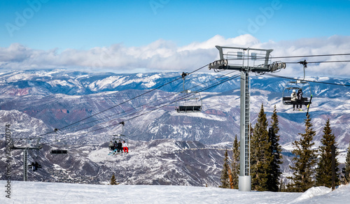 Skiers and snowboarders ascend the Elk Camp chairlift at the Aspen Snowmass ski resort, in the Rocky Mountains of Colorado on a partly cloudy winter day. © David A Litman