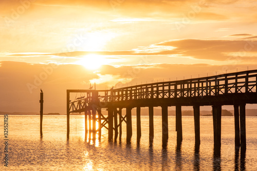 wooden dock with long walking path on the water with sun rising above the thick cloud over the horizon