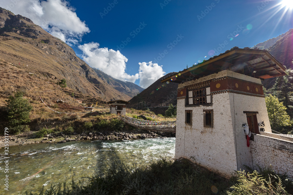 The Mountain landscape of Bhutan, the Paro Chu River beside the Paro - Thimphu Highway. A small Dzong on the fast flowing mountain river in the Himalayas. White clouds on a clear blue sky. 