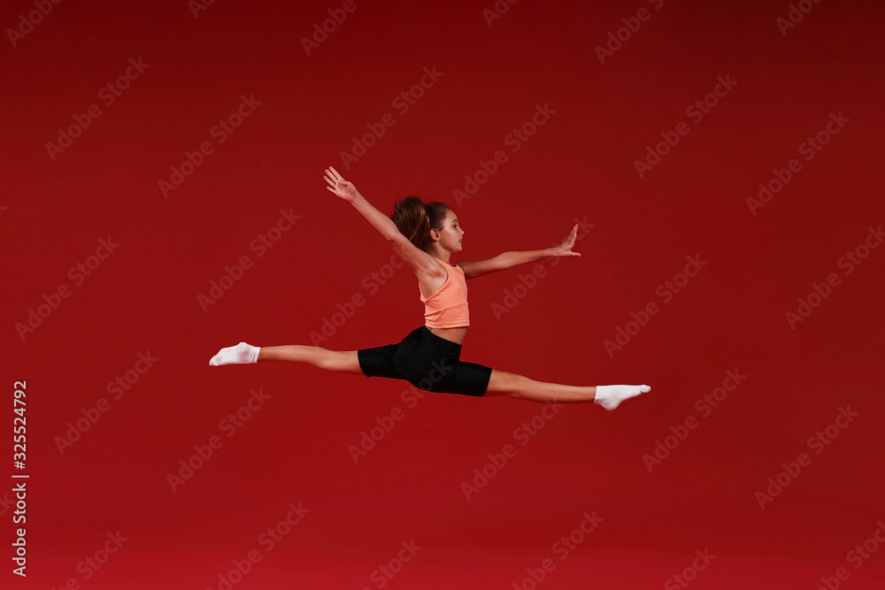 Be the Best. A cute kid, girl is engaged in sport, she is in motion jumping over in the air. Isolated on red background. Fitness, training, active lifestyle concept. Horizontal shot Be the Best. A cute kid, girl is engaged in sport, she is in motion jumping over in the air. Isolated on red background. Fitness, training, active lifestyle concept. Horizontal shot