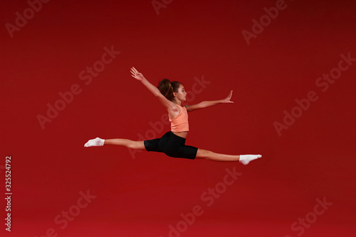 Be the Best. A cute kid, girl is engaged in sport, she is in motion jumping over in the air. Isolated on red background. Fitness, training, active lifestyle concept. Horizontal shot
