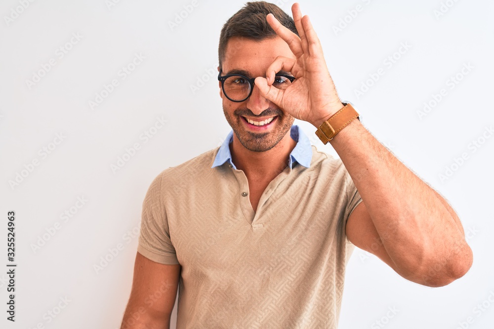 Naklejka premium Young handsome man wearing glasses over isolated background doing ok gesture with hand smiling, eye looking through fingers with happy face.