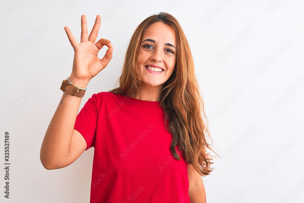 Young redhead woman wearing red casual t-shirt stading over white isolated background smiling positive doing ok sign with hand and fingers. Successful expression. Young redhead woman wearing red casual t-shirt stading over white isolated background smiling positive doing ok sign with hand and fingers. Successful expression.