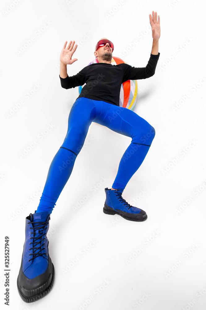 Portrait of athletic man with muscular legs exercising with beach ball over white studio background.