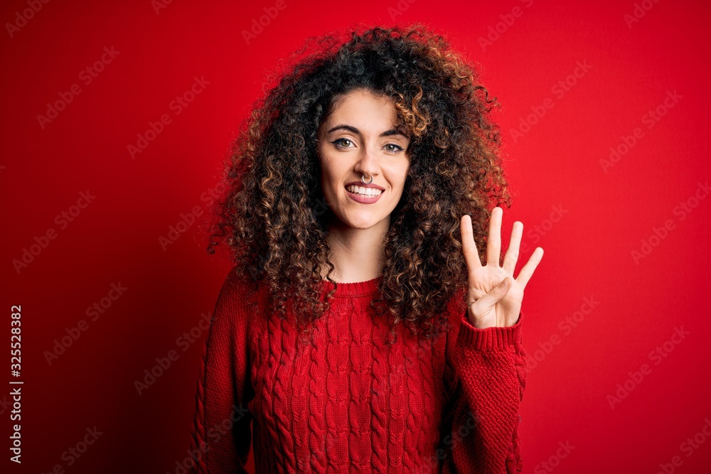 Young beautiful woman with curly hair and piercing wearing casual red sweater showing and pointing up with fingers number four while smiling confident and happy. Young beautiful woman with curly hair and piercing wearing casual red sweater showing and pointing up with fingers number four while smiling confident and happy.
