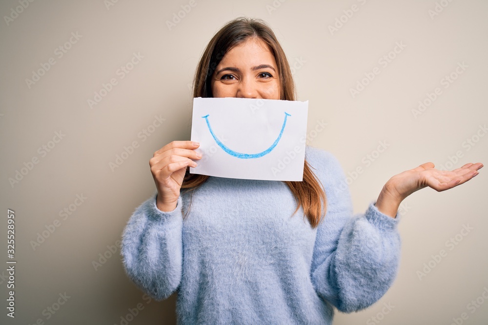Young blonde woman holding funny smile drawing on mouth as happy expression very happy and excited, winner expression celebrating victory screaming with big smile and raised hands Young blonde woman holding funny smile drawing on mouth as happy expression very happy and excited, winner expression celebrating victory screaming with big smile and raised hands