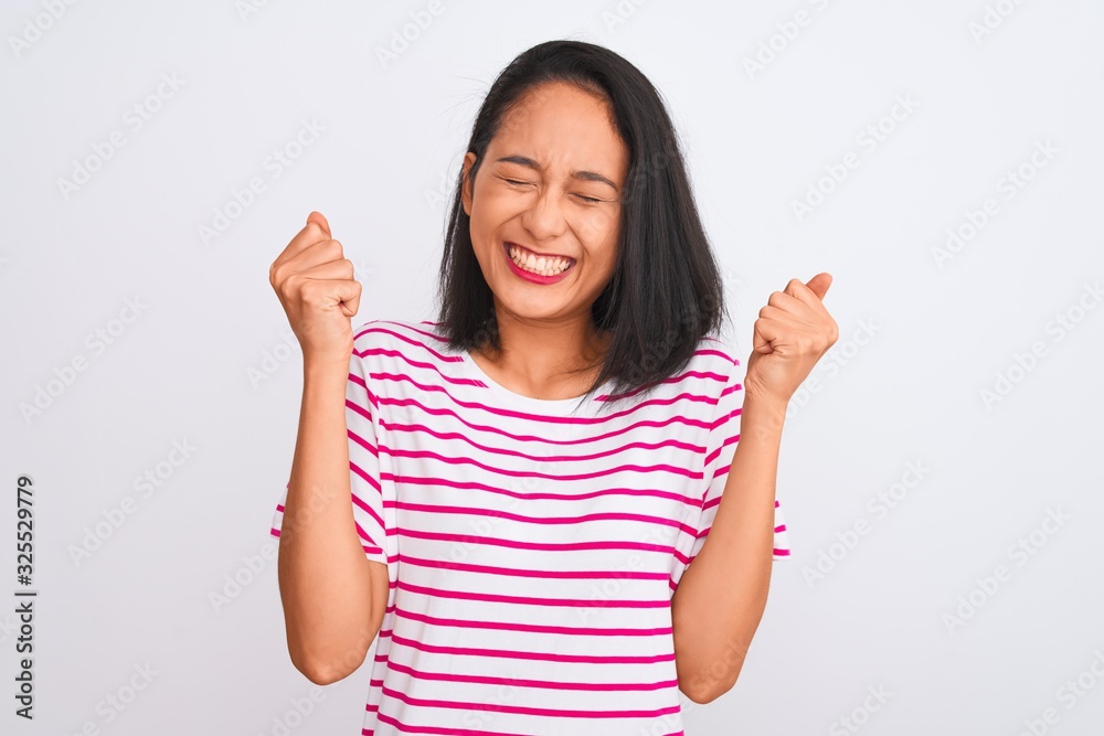 Young chinese woman wearing striped t-shirt standing over isolated white background excited for success with arms raised and eyes closed celebrating victory smiling. Winner concept. Young chinese woman wearing striped t-shirt standing over isolated white background excited for success with arms raised and eyes closed celebrating victory smiling. Winner concept.
