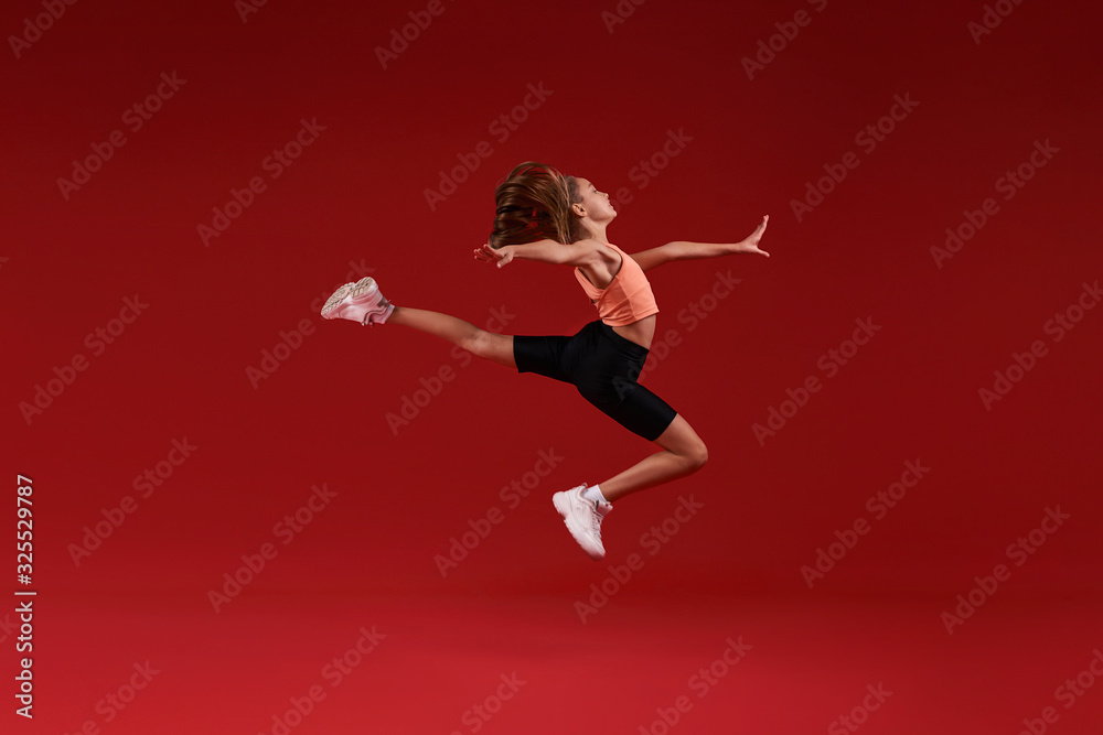 Do your best. A cute kid, girl is engaged in sport, she is in motion jumping over in the air. Isolated on red background. Fitness, training, active lifestyle concept. Horizontal shot