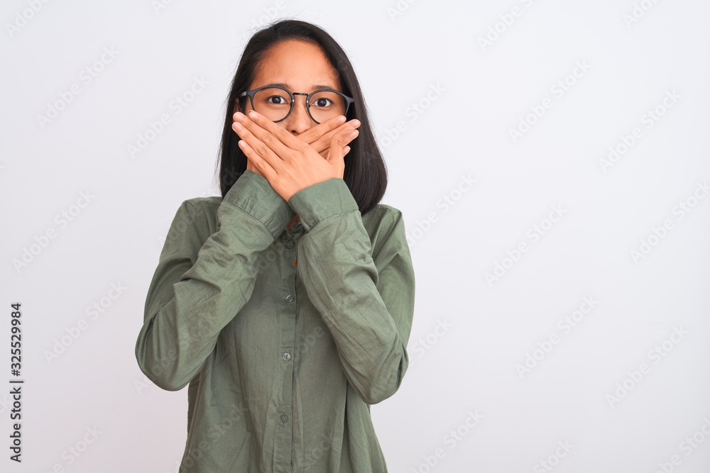 Young chinese woman wearing green shirt and glasses over isolated white background shocked covering mouth with hands for mistake. Secret concept. Young chinese woman wearing green shirt and glasses over isolated white background shocked covering mouth with hands for mistake. Secret concept.