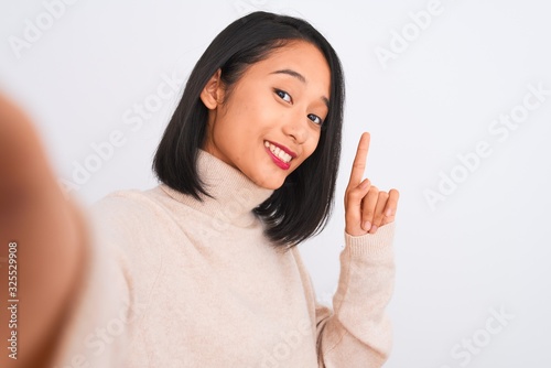 Young chinese woman wearing turtleneck sweater make selfie over isolated white background surprised with an idea or question pointing finger with happy face, number one