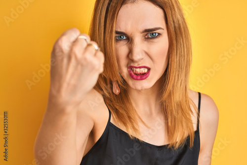 Close up of caucasian elegant woman over isolated yellow background annoyed and frustrated shouting with anger, crazy and yelling with raised hand, anger concept