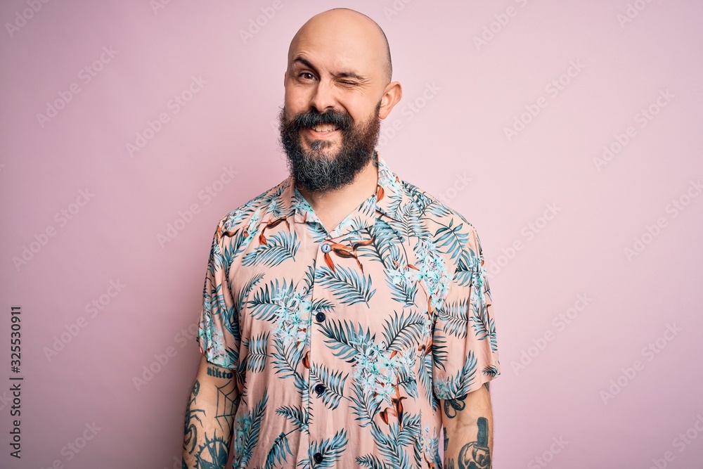 Handsome bald man with beard and tattoo wearing casual floral shirt over  pink background winking looking at the camera with sexy expression,  cheerful and happy face. Stock Photo | Adobe Stock
